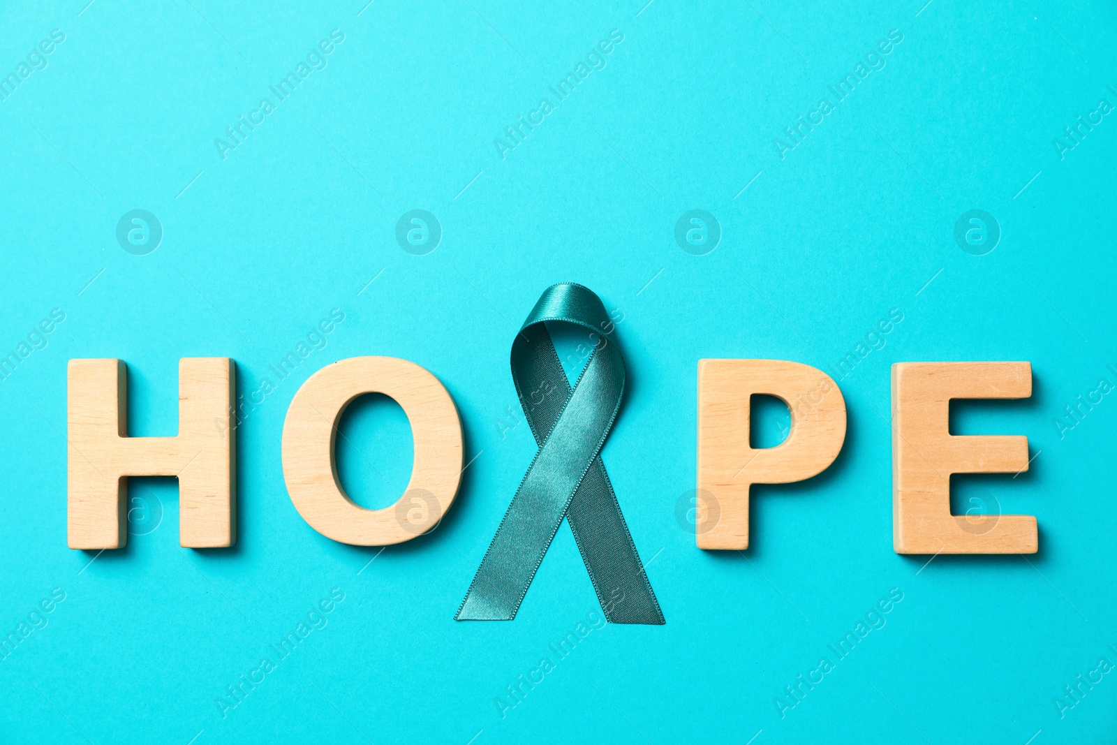 Photo of Word Hope made of wooden letters and teal awareness ribbon on light blue background. Symbol of social and medical issues