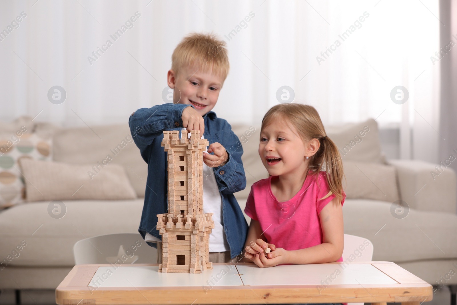 Photo of Little girl and boy playing with wooden tower at table indoors. Children's toy