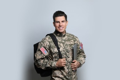 Photo of Cadet with backpack and laptop on light grey background. Military education