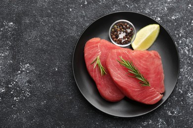 Raw tuna fillets with rosemary, spices and lime wedge on black table, top view. Space for text
