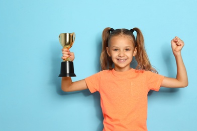 Photo of Happy girl with golden winning cup on blue background