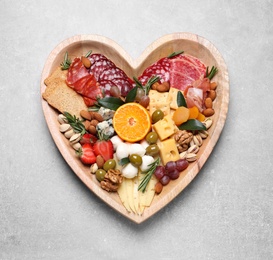Heart shaped plate with different delicious snacks on grey table, top view