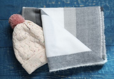 Soft scarf and knitted hat on blue wooden table, top view