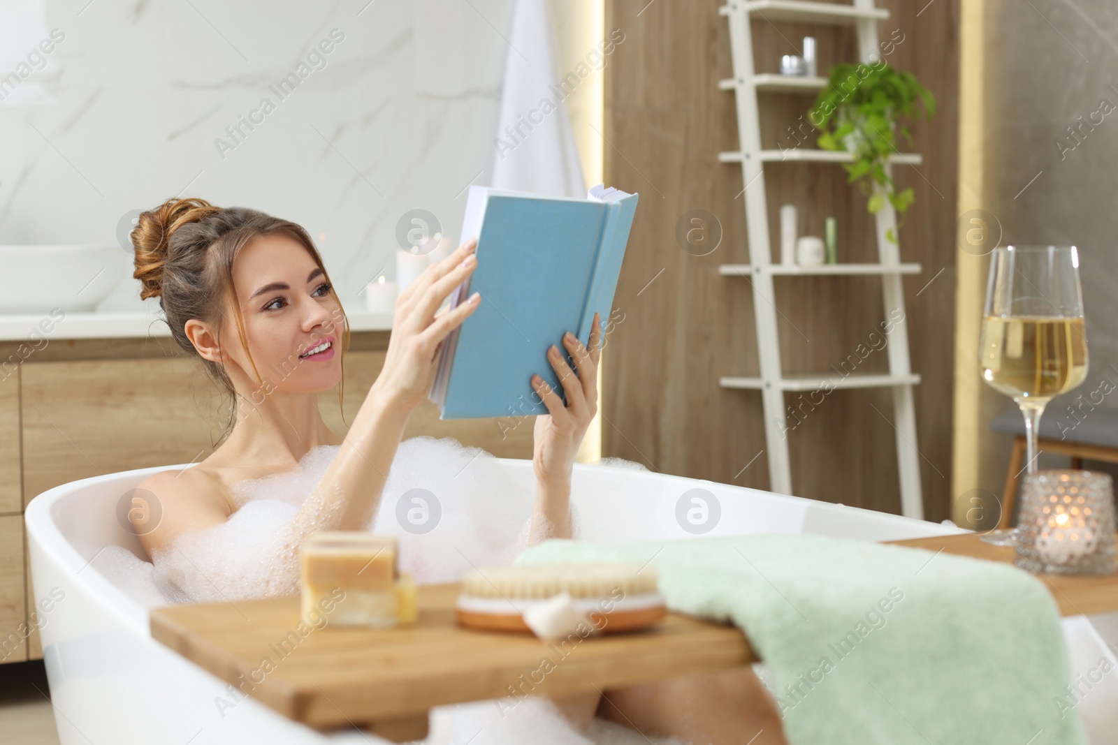 Photo of Beautiful woman reading book while enjoying bubble bath at home