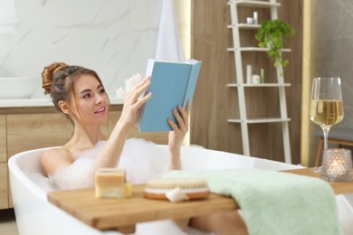 Beautiful woman reading book while enjoying bubble bath at home