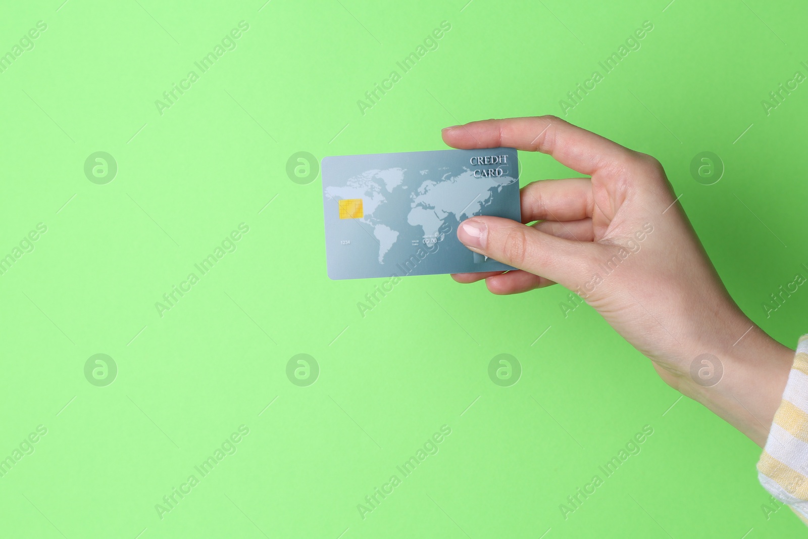 Photo of Woman holding credit card on light green background, closeup