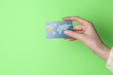 Woman holding credit card on light green background, closeup