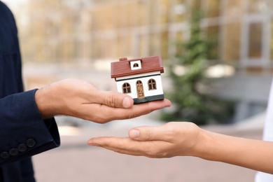 Male real estate agent giving house model to woman outdoors, closeup