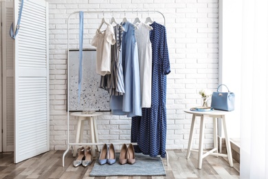 Photo of Wardrobe rack with women's clothes and different shoes at white brick wall in room