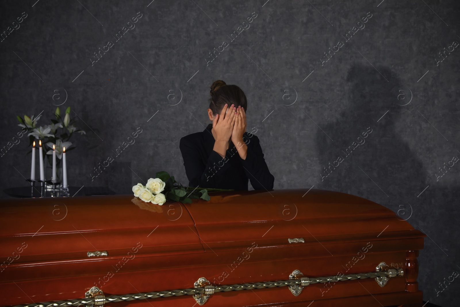 Photo of Sad young woman mourning near casket with white roses in funeral home