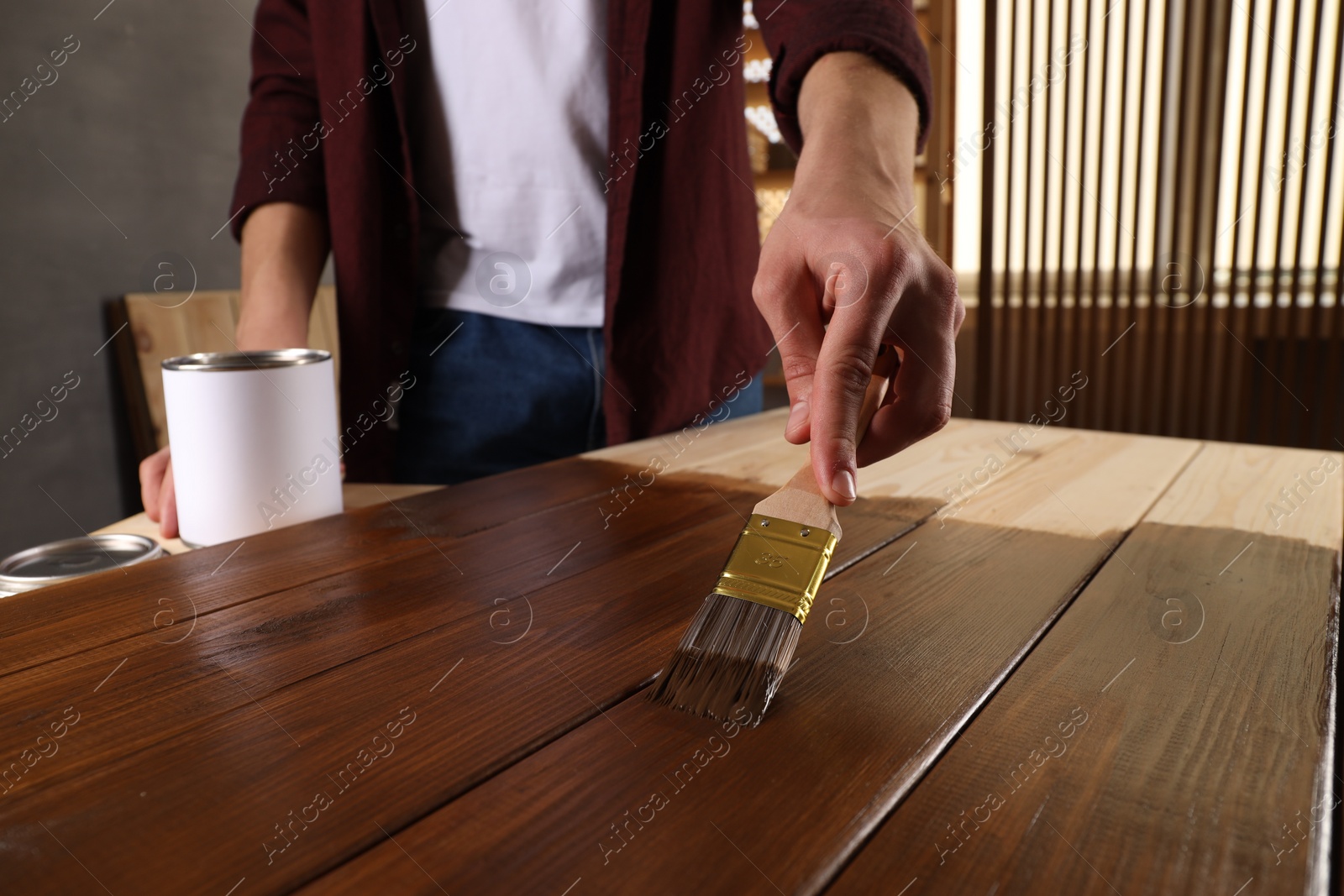 Photo of Man with brush applying wood stain onto wooden surface indoors, closeup