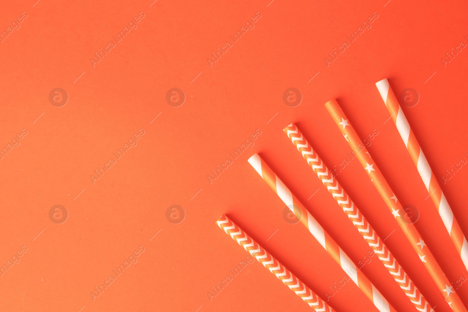 Photo of Striped paper drinking straws on orange background, flat lay. Space for text