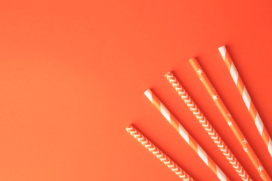 Photo of Striped paper drinking straws on orange background, flat lay. Space for text