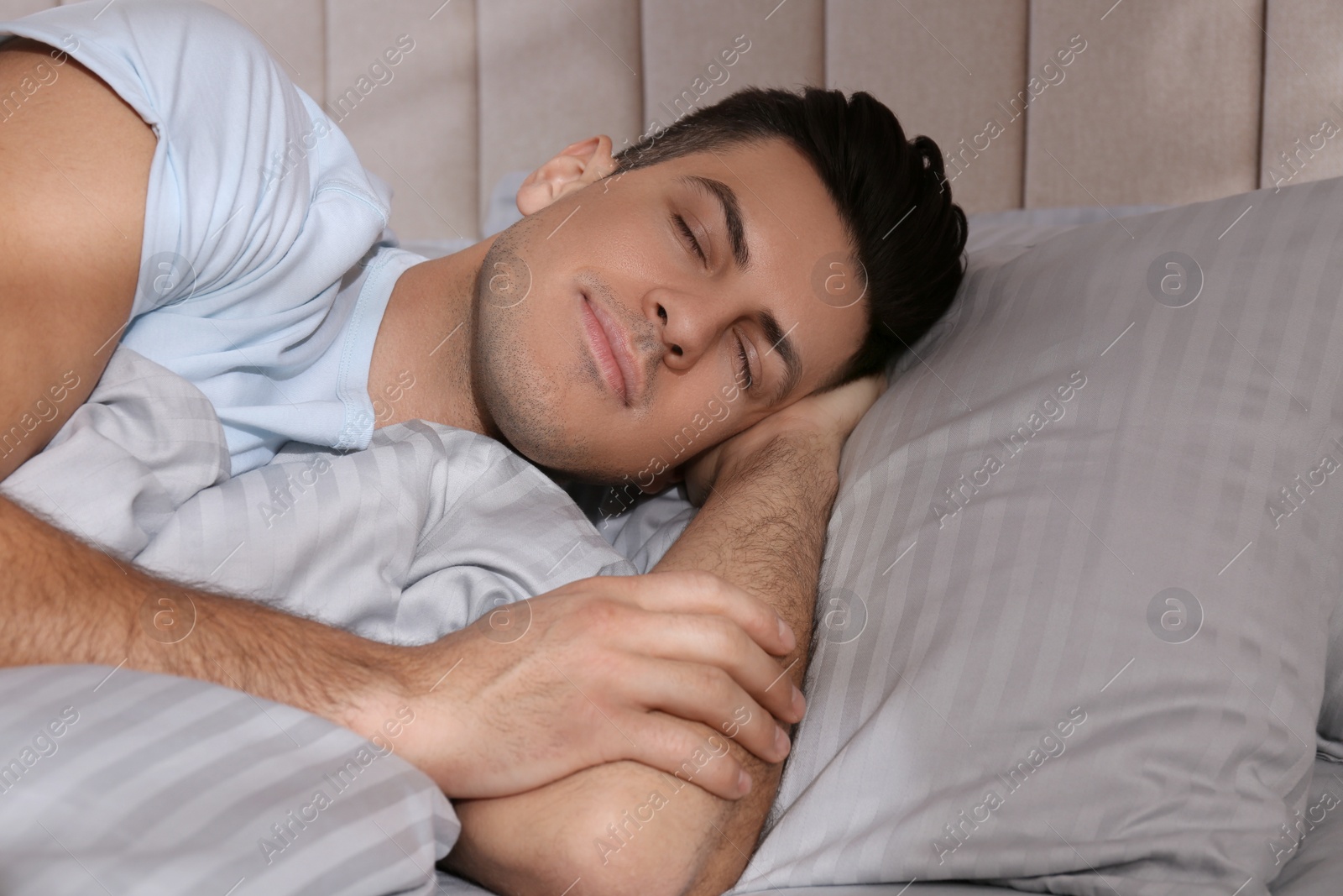 Photo of Man sleeping in comfortable bed with light grey striped linens