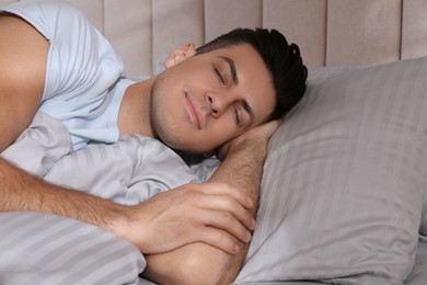 Man sleeping in comfortable bed with light grey striped linens