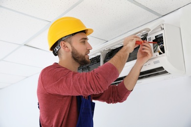 Photo of Electrician with screwdriver repairing air conditioner indoors