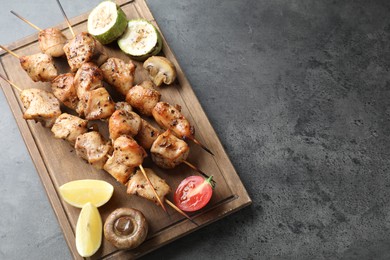 Delicious shish kebabs with vegetables and lemon on grey table, top view. Space for text