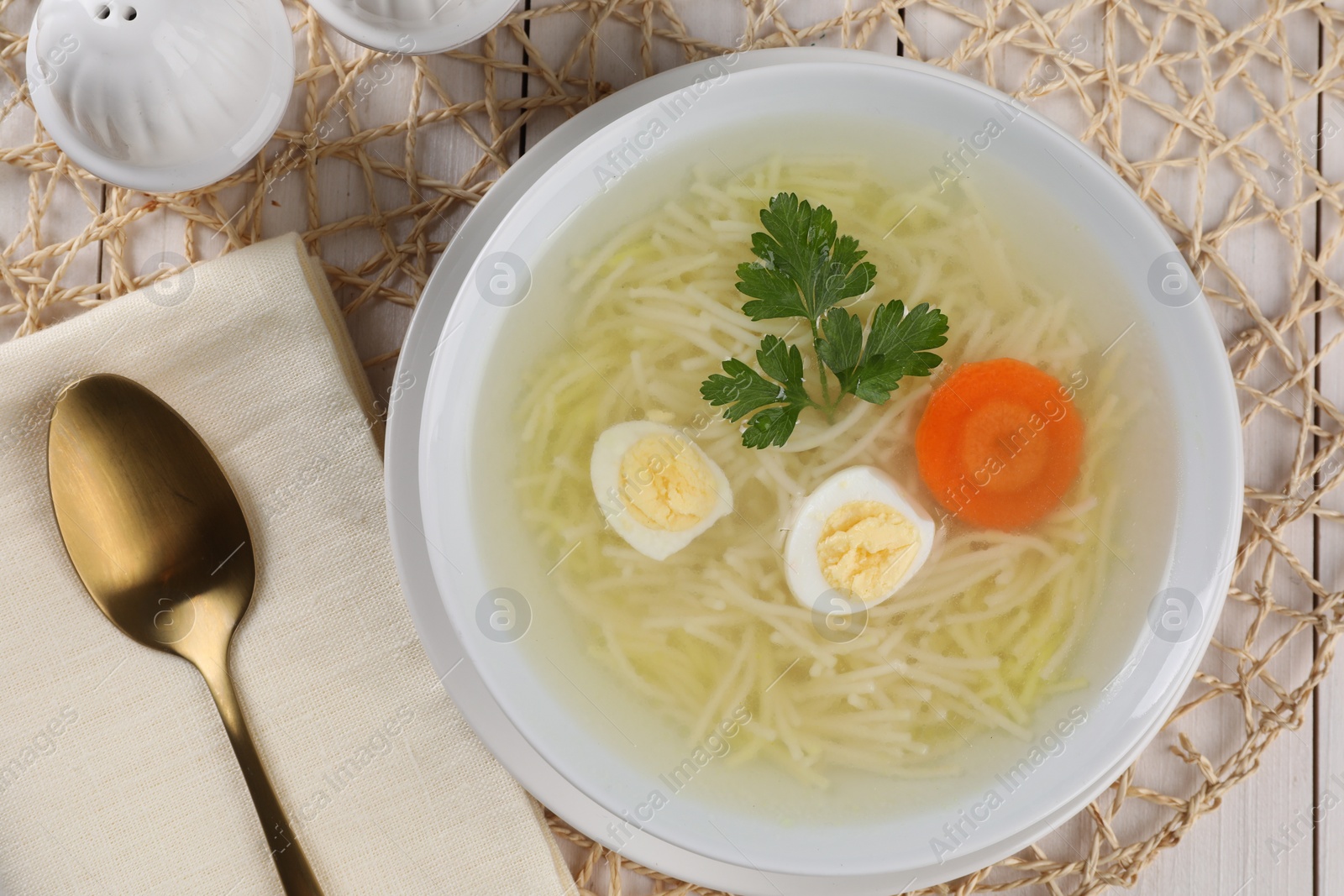 Photo of Tasty soup with noodles, egg, carrot and parsley in bowl served on white wooden table, flat lay