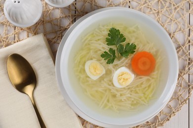 Photo of Tasty soup with noodles, egg, carrot and parsley in bowl served on white wooden table, flat lay