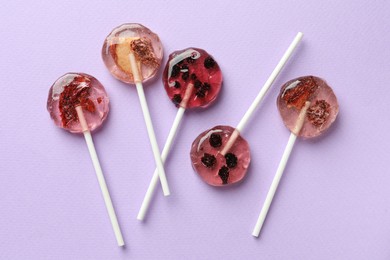 Photo of Sweet colorful lollipops with berries on lilac background, flat lay