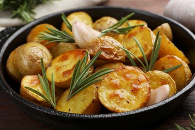 Photo of Delicious baked potatoes with rosemary in frying pan, closeup