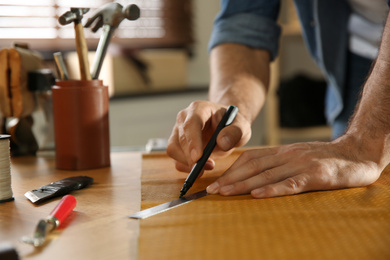 Photo of Man working with piece of leather in workshop, closeup