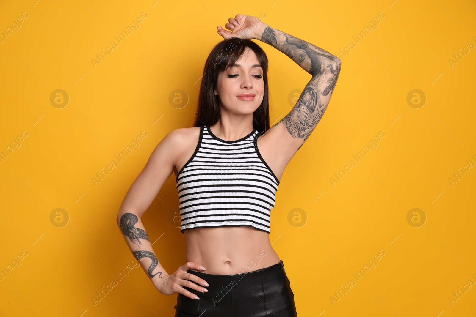 Photo of Beautiful woman with tattoos on arms against yellow background