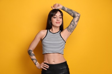 Beautiful woman with tattoos on arms against yellow background