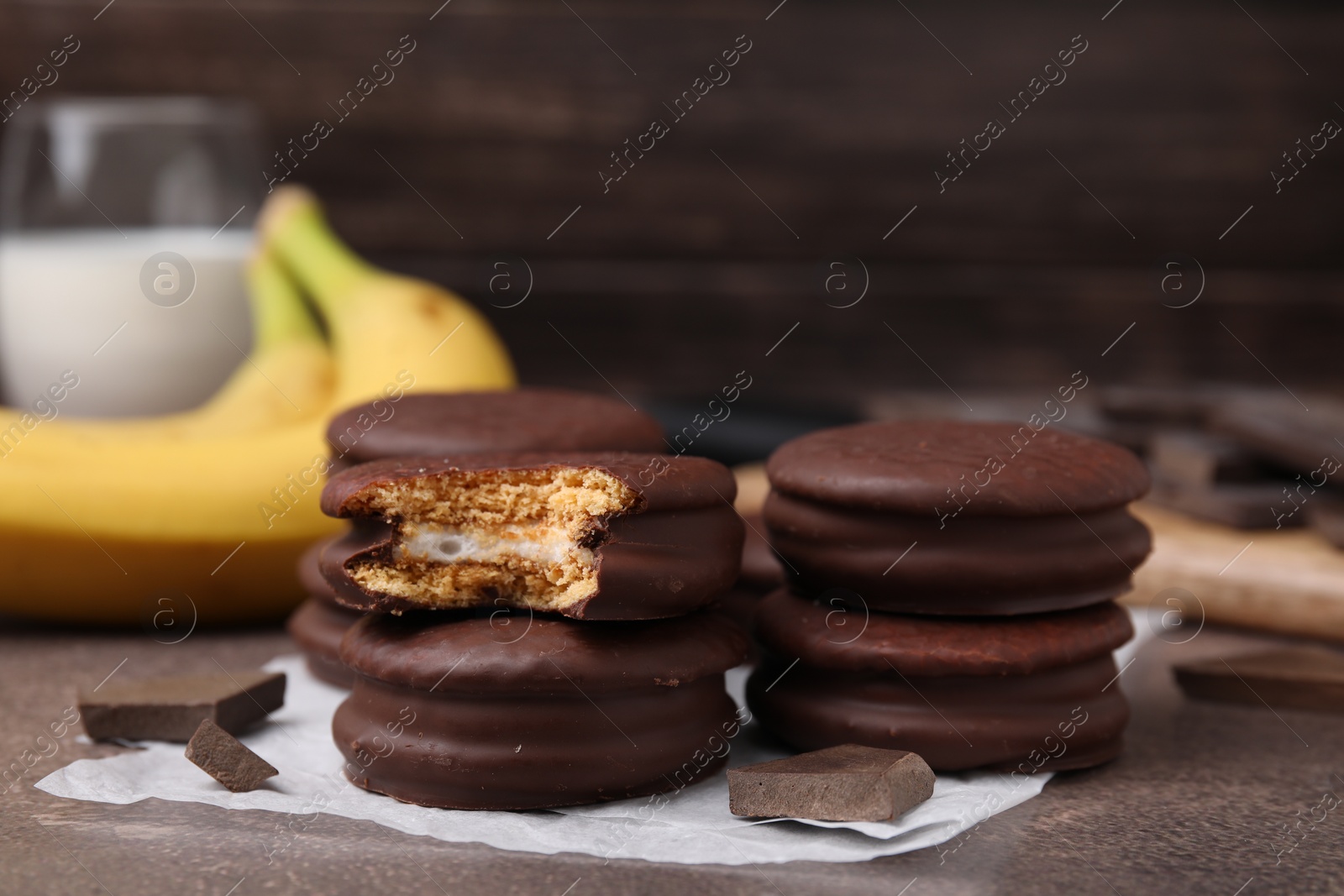 Photo of Tasty banana choco pies and pieces of chocolate on textured table, closeup