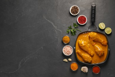 Photo of Tasty chicken curry and ingredients on black textured table, flat lay. Space for text