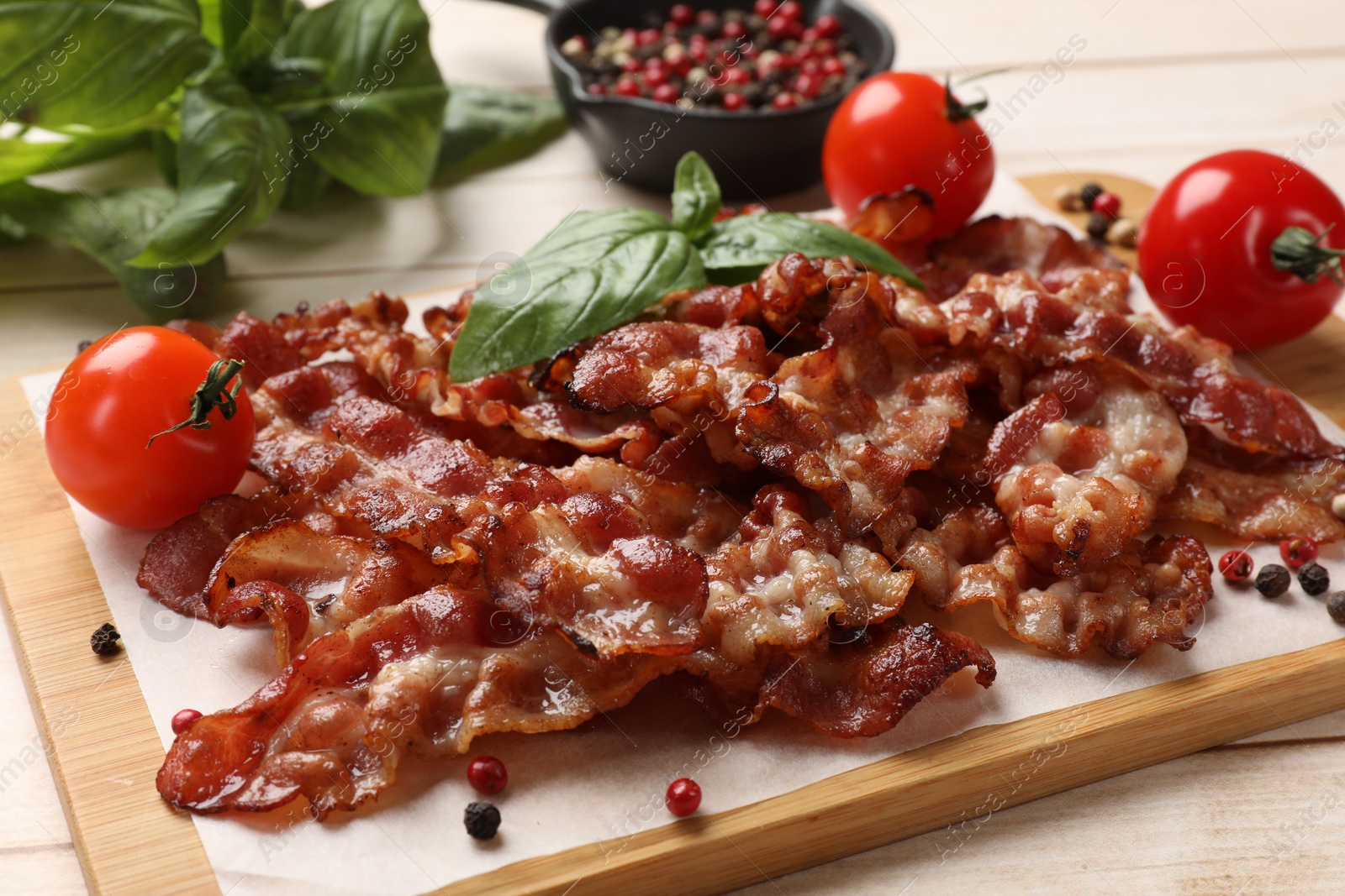 Photo of Slices of tasty fried bacon with different spices and tomatoes on wooden table, closeup