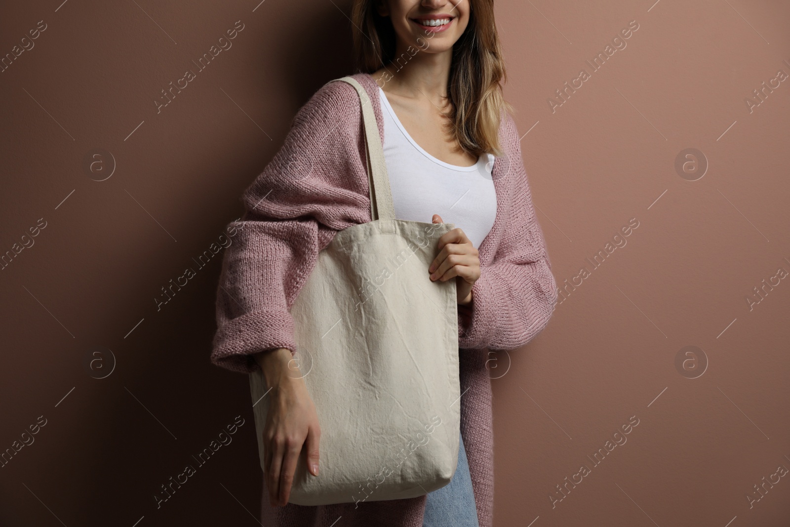 Photo of Happy young woman with blank eco friendly bag against light brown background, closeup