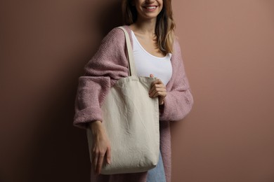 Happy young woman with blank eco friendly bag against light brown background, closeup