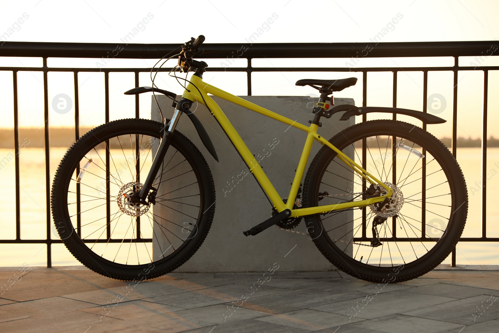 Photo of Yellow bicycle parked near railing on city waterfront at sunset