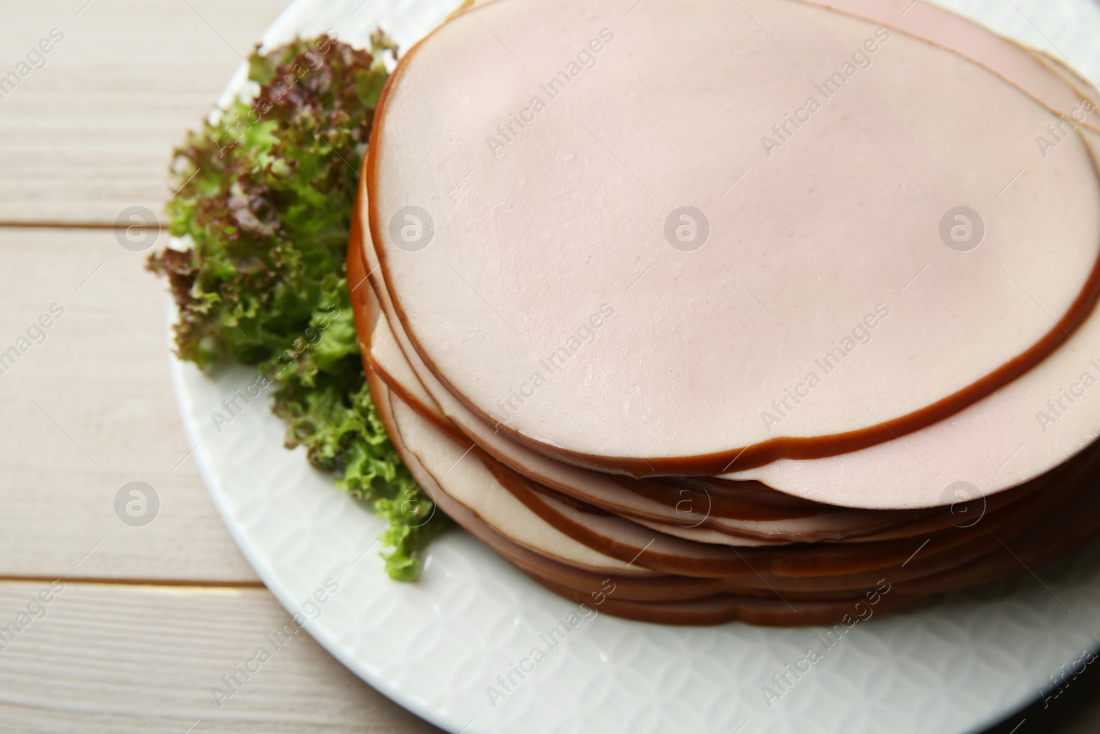 Photo of Slices of delicious boiled sausage with lettuce on beige wooden table, above view