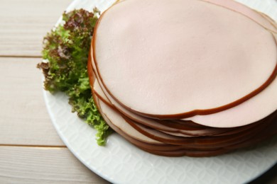 Slices of delicious boiled sausage with lettuce on beige wooden table, above view