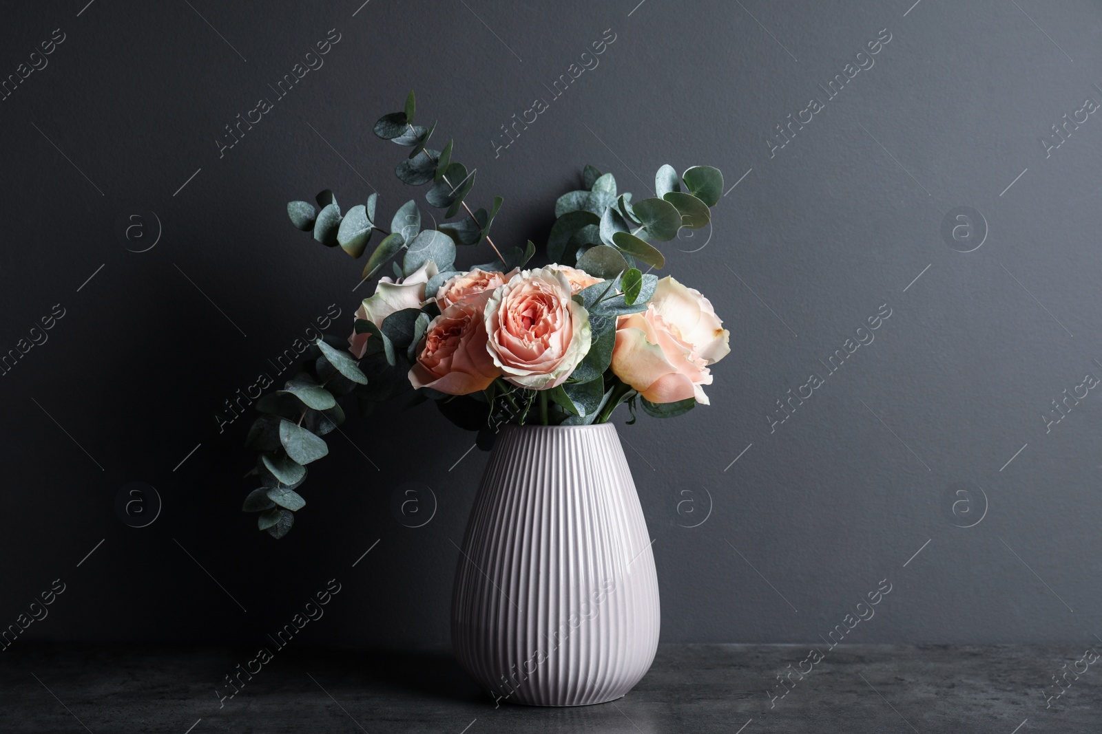 Photo of Bouquet of beautiful flowers and eucalyptus branches in vase on table against black background