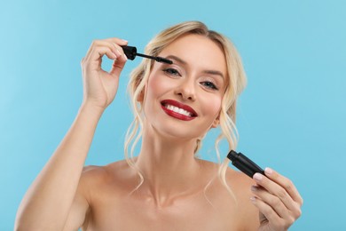 Photo of Beautiful makeup. Smiling woman applying mascara on light blue background