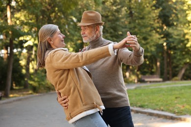 Photo of Affectionate senior couple dancing together in park. Romantic date