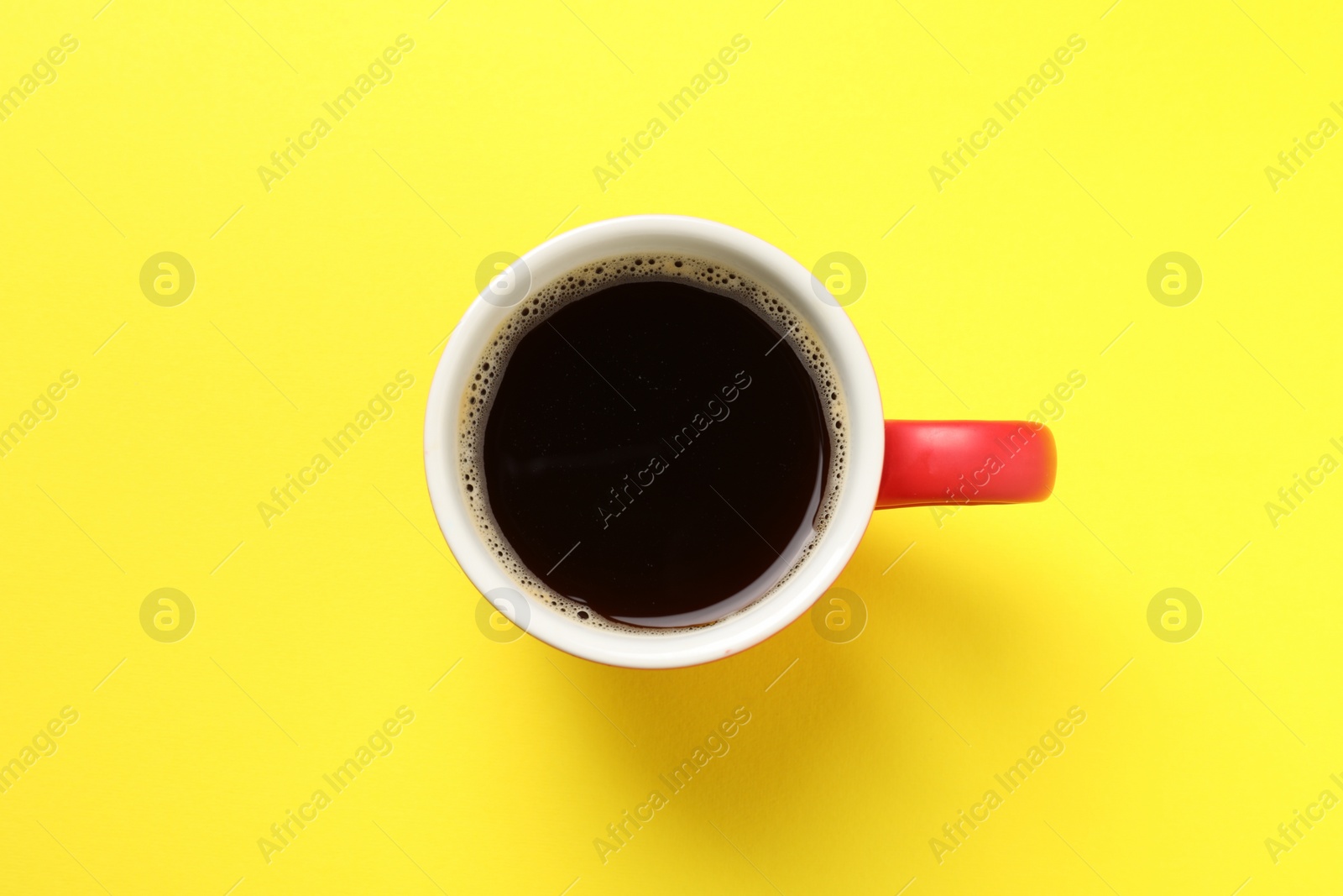 Photo of Aromatic coffee in cup on yellow background, top view