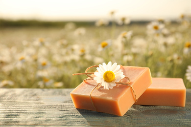 Photo of Chamomile soap bars on blue wooden table in field