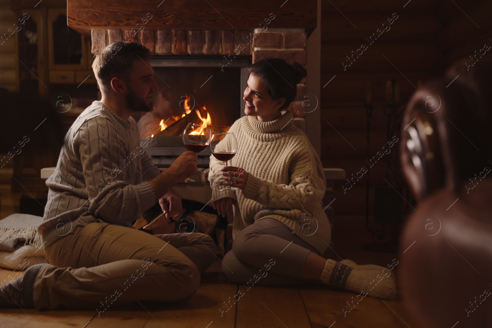 Photo of Lovely couple with glasses of wine near fireplace at home. Winter vacation