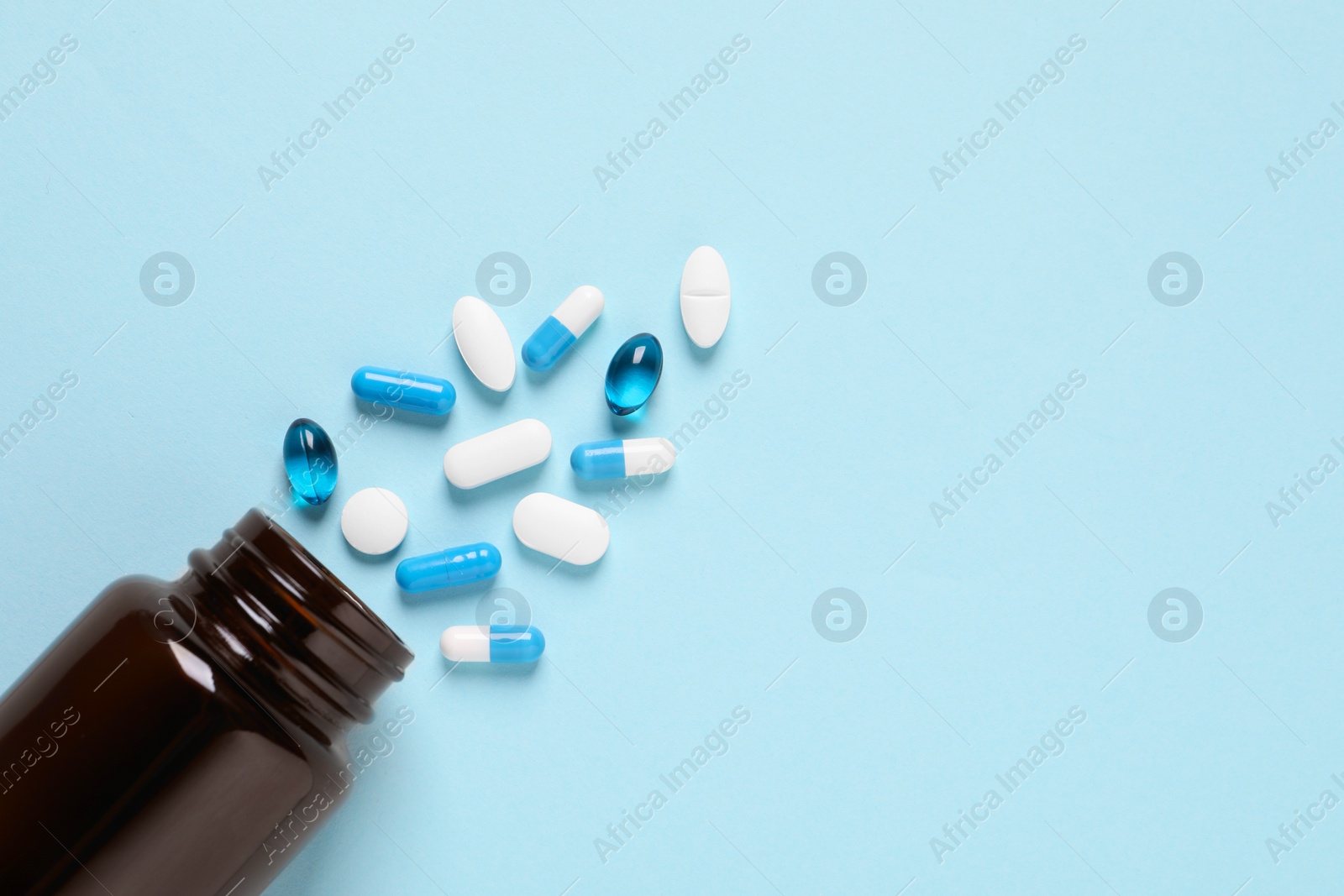 Photo of Plastic bottle with many different pills on light blue background, flat lay. Space for text