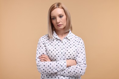 Portrait of sad woman with crossed arms on beige background