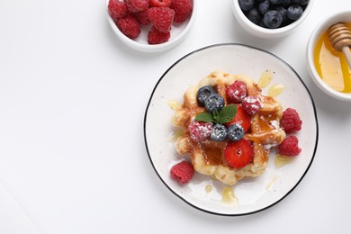 Photo of Delicious Belgian waffle with fresh berries and honey on white table, flat lay. Space for text