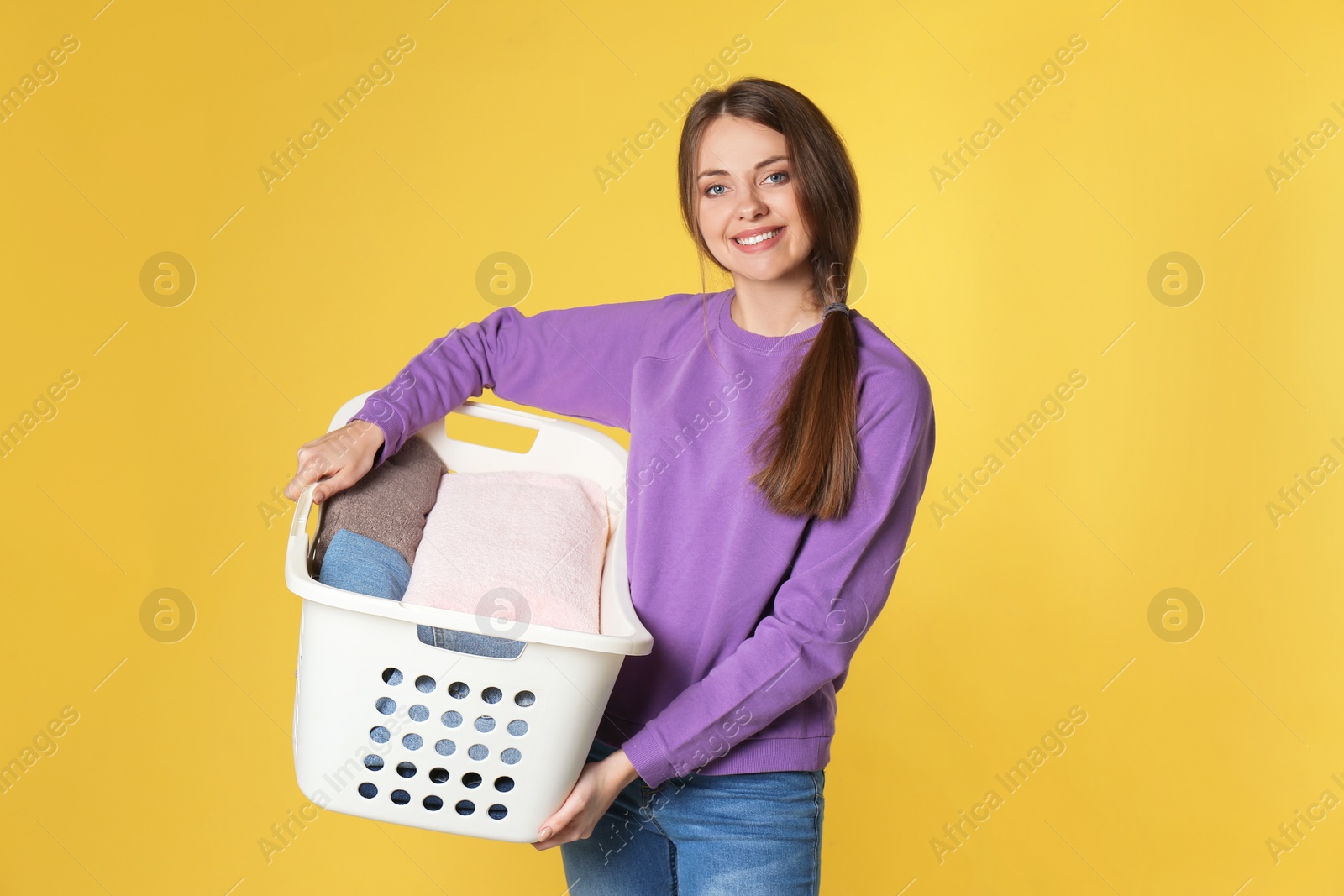Photo of Happy young woman holding basket with laundry on color background