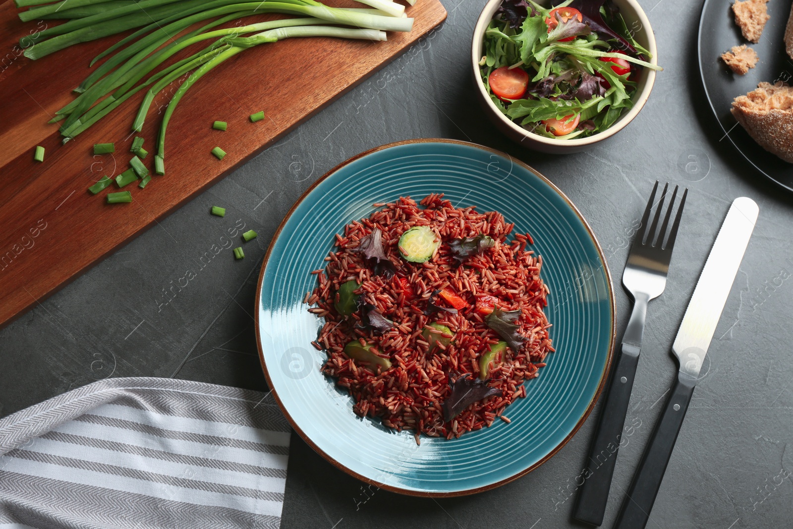 Photo of Tasty brown rice with vegetables served on dark grey table, flat lay