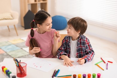 Photo of Happy brother and sister drawing at white table in room