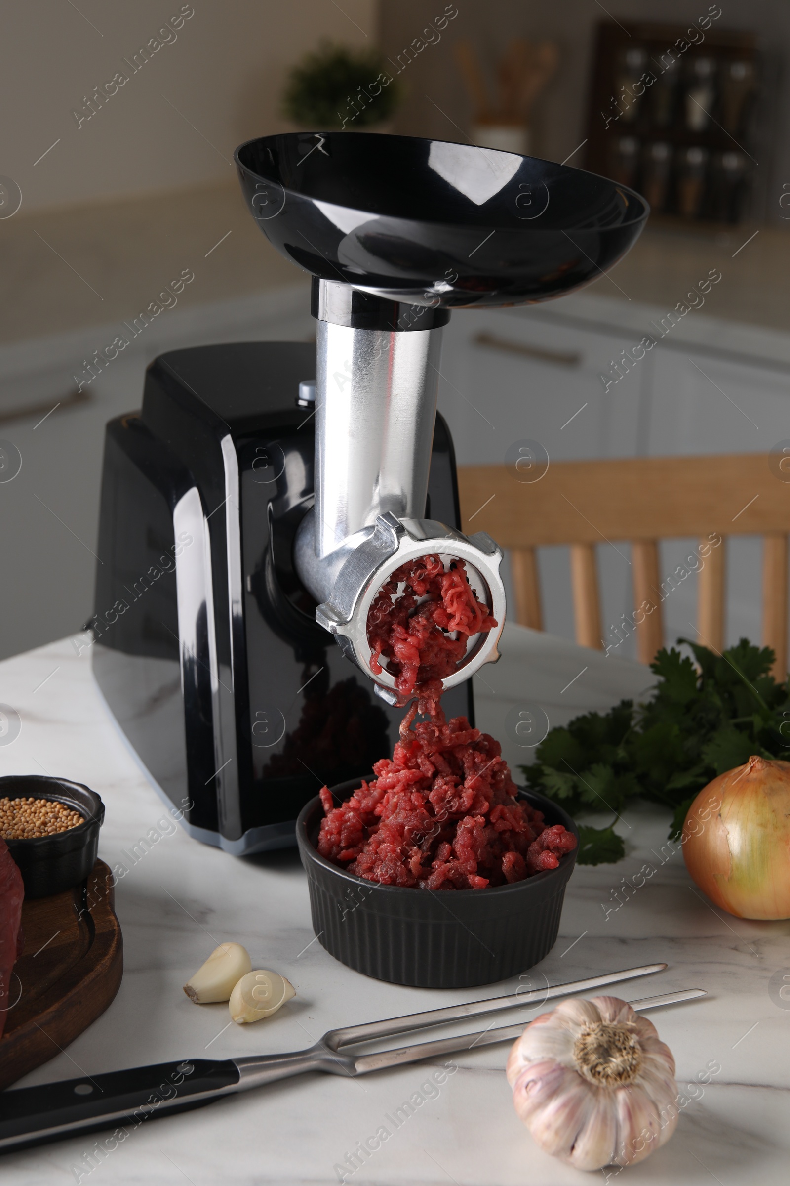 Photo of Electric meat grinder with beef mince and products on white marble table in kitchen