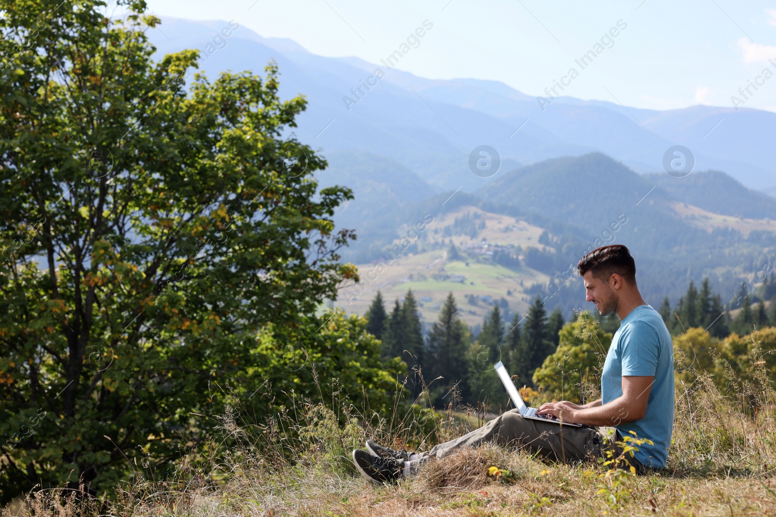Photo of Man working with laptop outdoors surrounded by beautiful nature. Space for text